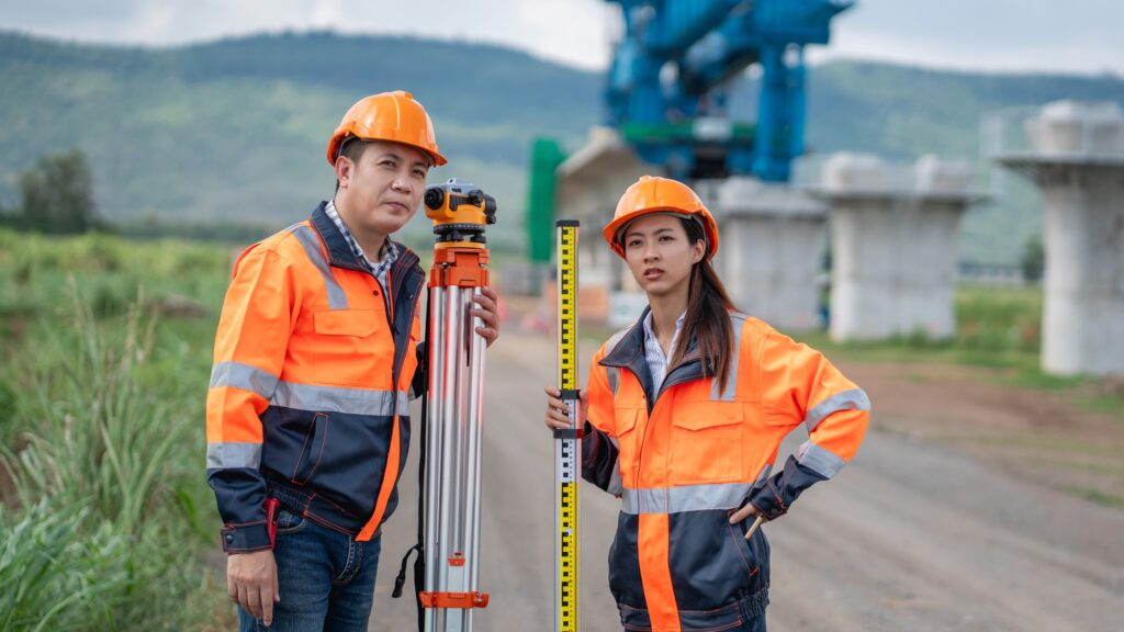 The survey team is using a theodolite and road construction plans.