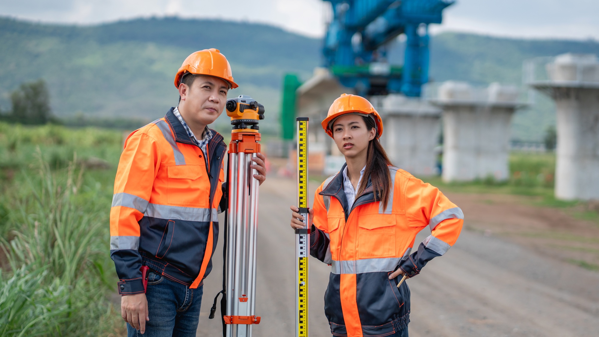 The survey team is using a theodolite and road construction plans.
